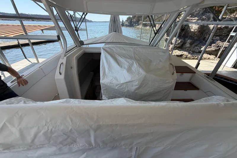  Yacht Photos Pics 2023 Regal 38 SAV boat interior with protective covers, docked by a scenic shoreline.