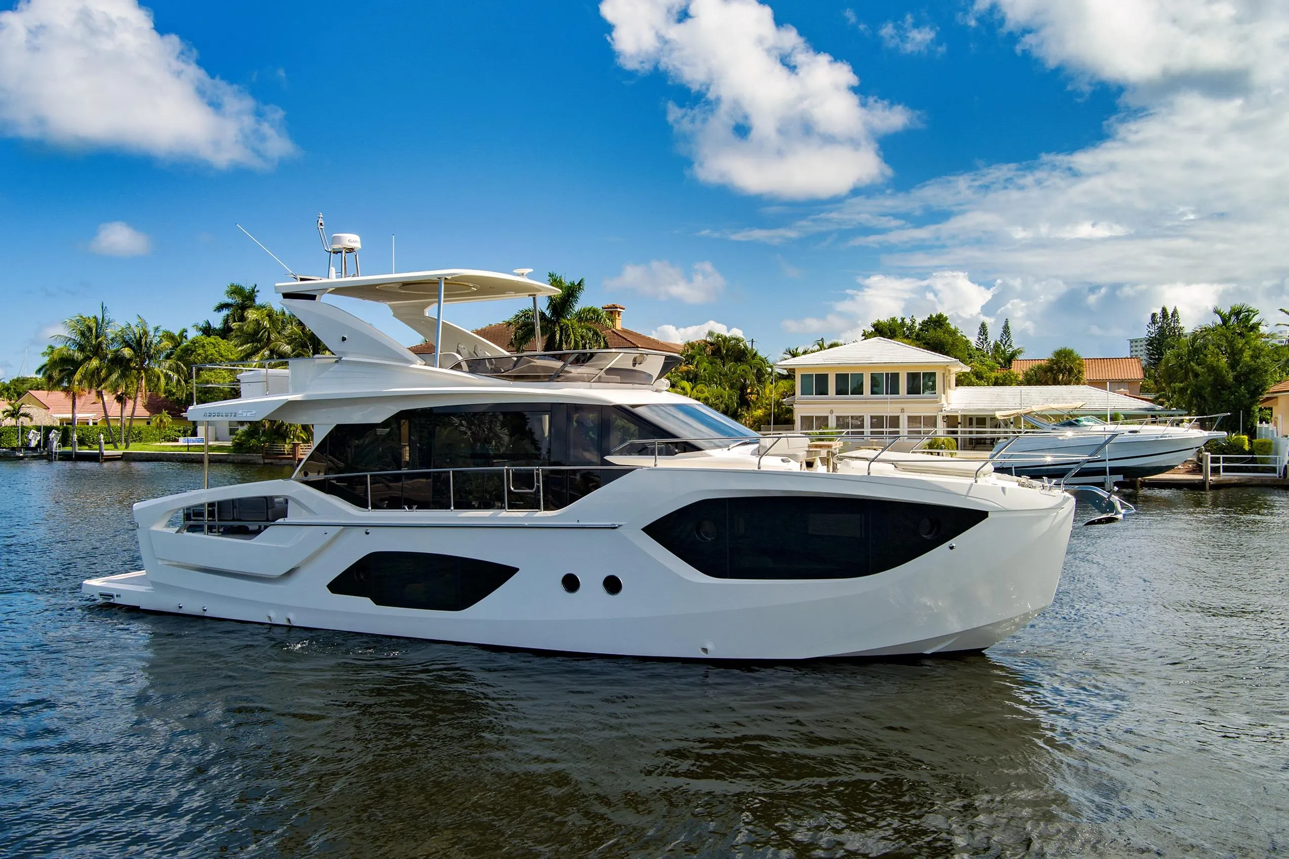 2025 Absolute 52 FLY yacht cruising on a sunny day near waterfront homes.