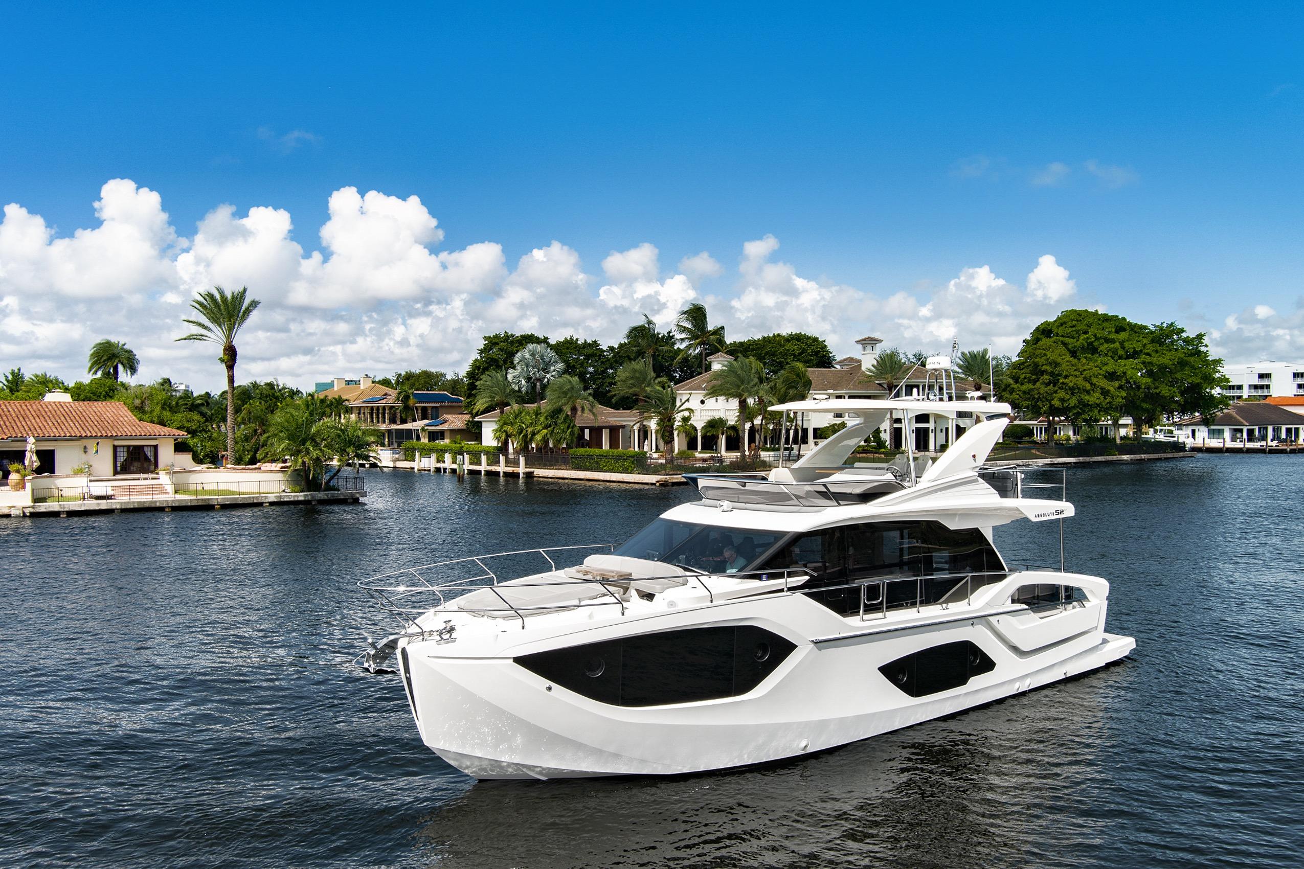 Luxury 2025 Absolute 52 FLY yacht cruising on a scenic waterfront with palm trees.
