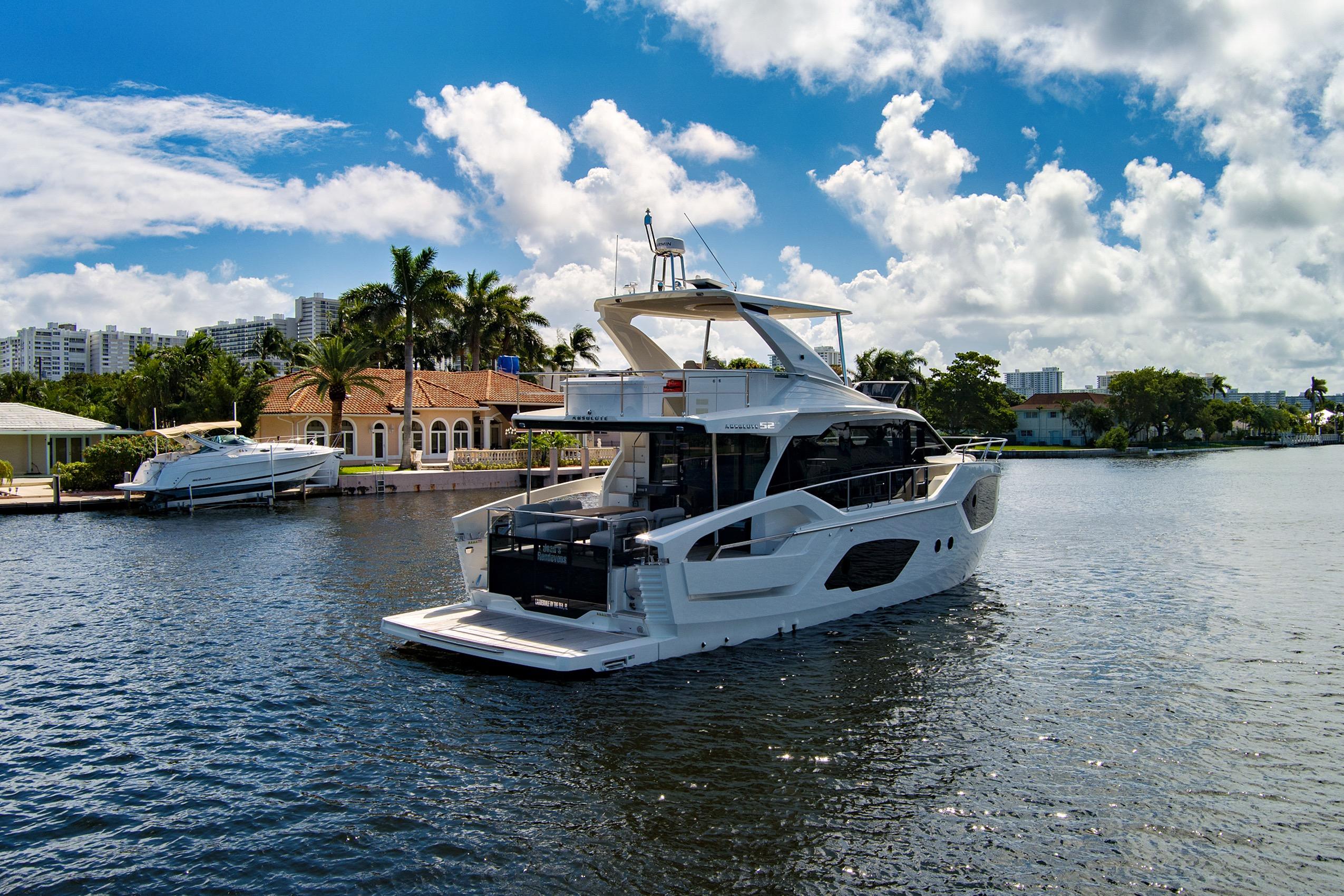 2025 Absolute 52 FLY yacht cruising on a sunny day near waterfront homes.