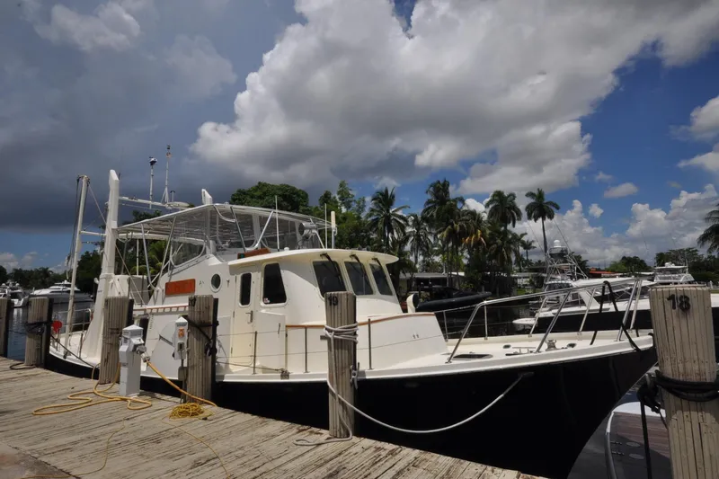  Yacht Photos Pics 1989 Seaton Trawler docked at marina under cloudy sky, surrounded by palm trees.