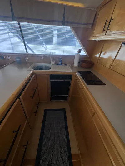 Hear After Yacht Photos Pics Compact kitchen in a 1995 Bertram 50 Convertible yacht with wooden cabinets and modern appliances.