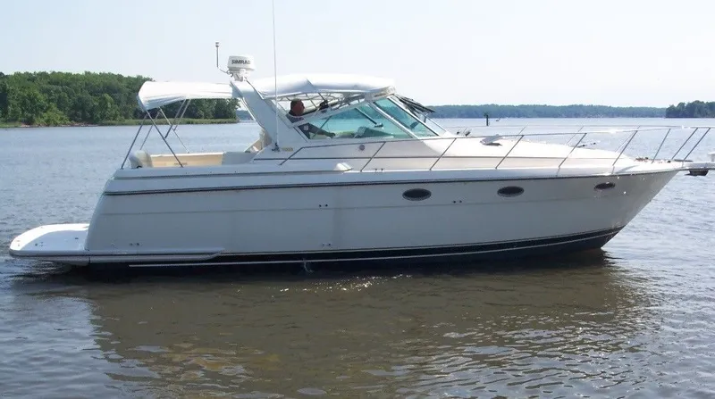 Why Knot Yacht Photos Pics 1996 Tiara Yachts 3500 Express cruising on a calm lake with forested shoreline.