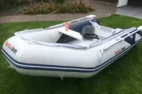 A white inflatable boat on grass, featuring a steering console and "honuWave" branding.