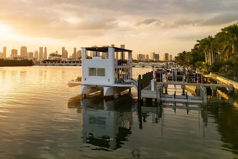  Yacht Photos Pics Floating modern houseboat, Arkup 50, docked at sunset with city skyline in background.