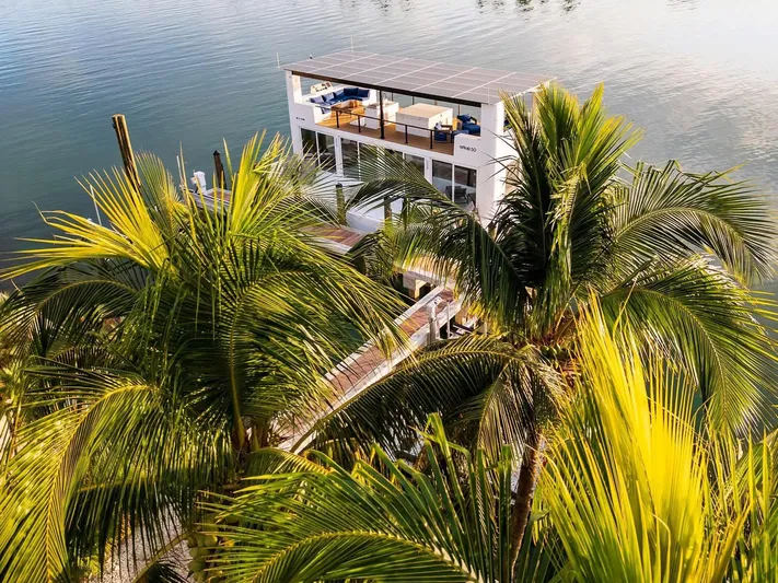  Yacht Photos Pics Floating luxury home Arkup 50 amidst lush palm trees on serene water.