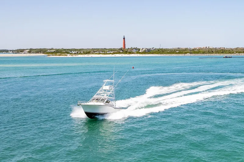 Patriot Yacht Photos Pics 2005 Carolina Classic 32 boat cruising on clear blue water near a distant lighthouse.