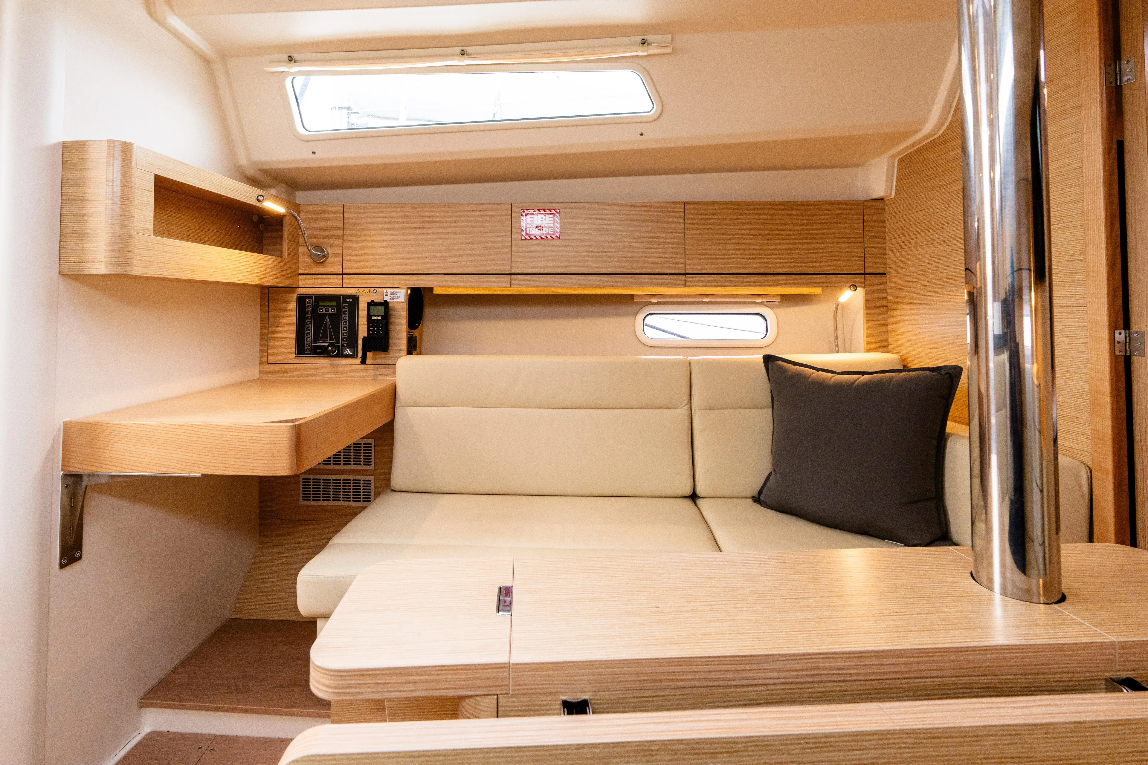 The Siren's Song Yacht Photos Pics 2023 Hanse 348 yacht interior with beige seating, wooden accents, and a small window.