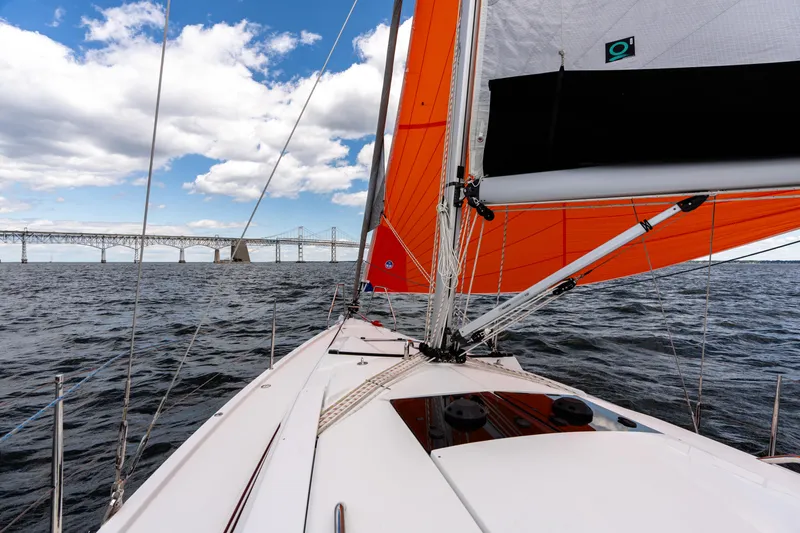 The Siren's Song Yacht Photos Pics Sailing on a 2023 Hanse 348 yacht with vibrant orange sails near a bridge.
