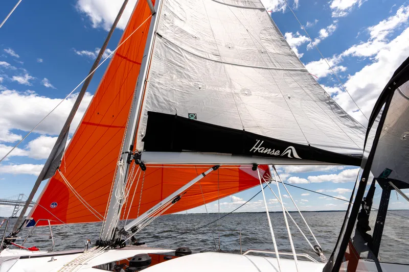 The Siren's Song Yacht Photos Pics 2023 Hanse 348 sailboat with vibrant orange sails on open water under blue sky.