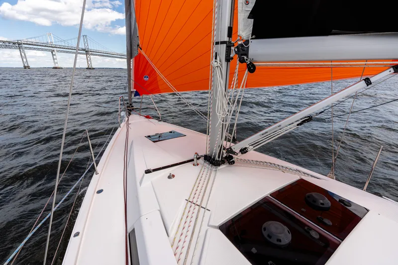 The Siren's Song Yacht Photos Pics 2023 Hanse 348 sailboat with orange sails on open water near a bridge.