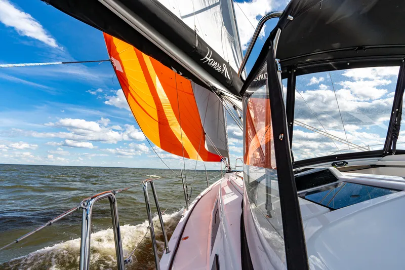 The Siren's Song Yacht Photos Pics 2023 Hanse 348 sailboat with vibrant orange sail on open water under blue sky.