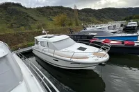 2023 Nimbus 305 Coupe docked in a scenic marina with lush hills.