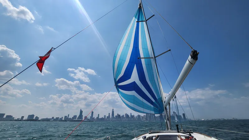 Superstition Yacht Photos Pics Sailing Beneteau Oceanis 40 with vibrant spinnaker against city skyline, clear blue sky.