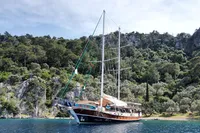 Custom 2007 GULET yacht anchored near lush, rocky coastline under a clear sky.