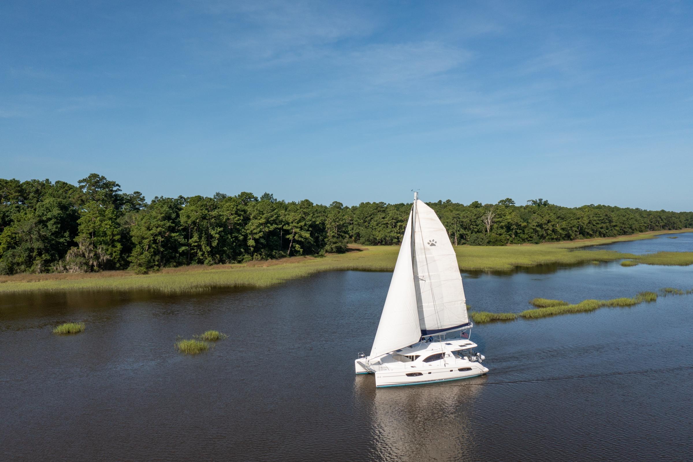 Sailing catamaran Leopard 44 cruising on a serene river, surrounded by lush greenery.