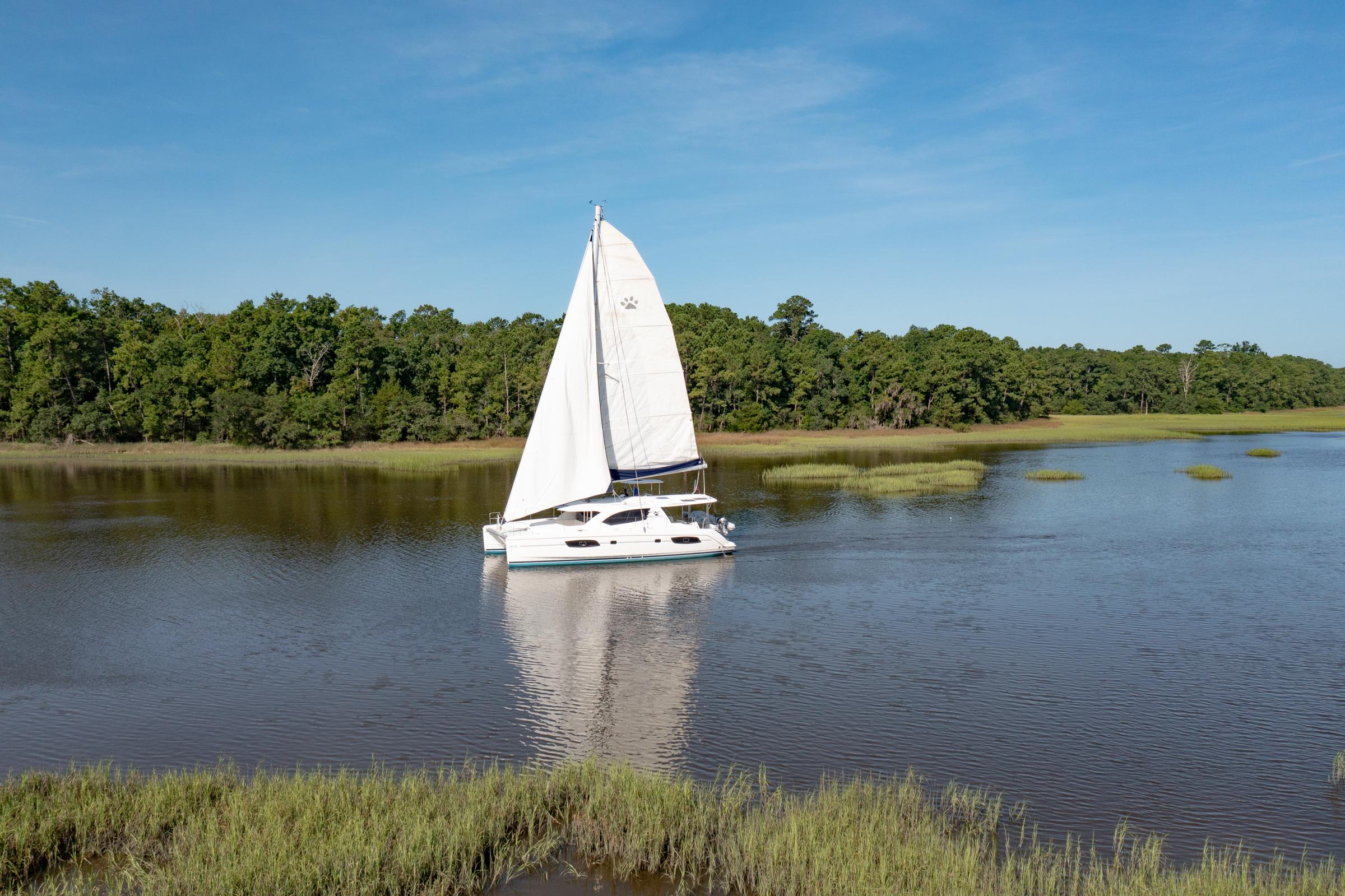 Sailing catamaran Leopard 44 Owners Version, 2016, on a serene river with lush greenery.