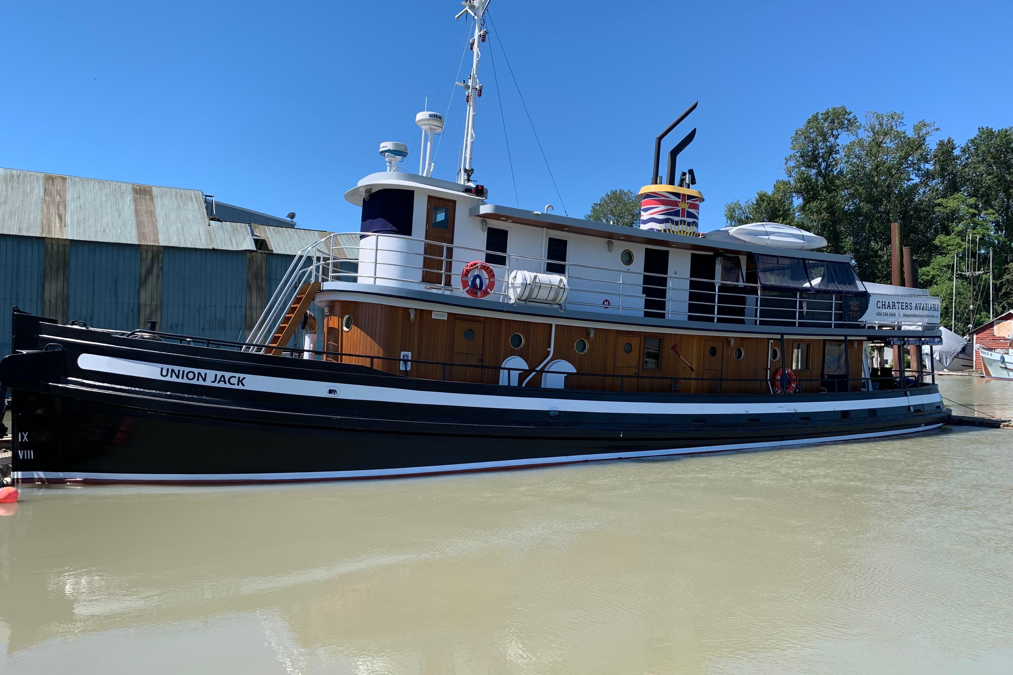 Historic 1941 McKenzie Barge & Derrick Co. Ltd tugboat "Union Jack" docked by a riverside warehouse.