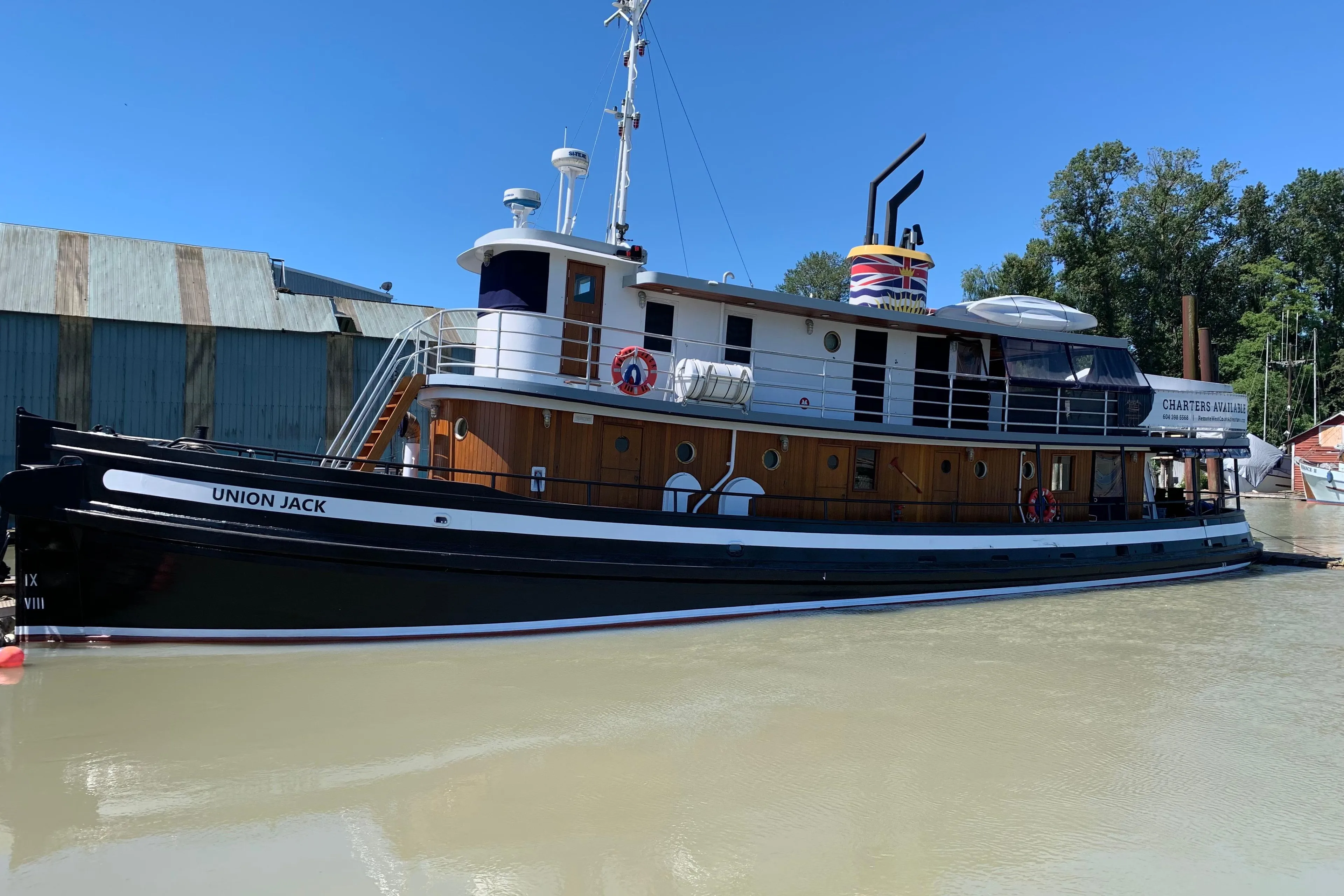 Historic 1941 McKenzie Barge & Derrick Co. Ltd tugboat "Union Jack" docked by a riverside warehouse.