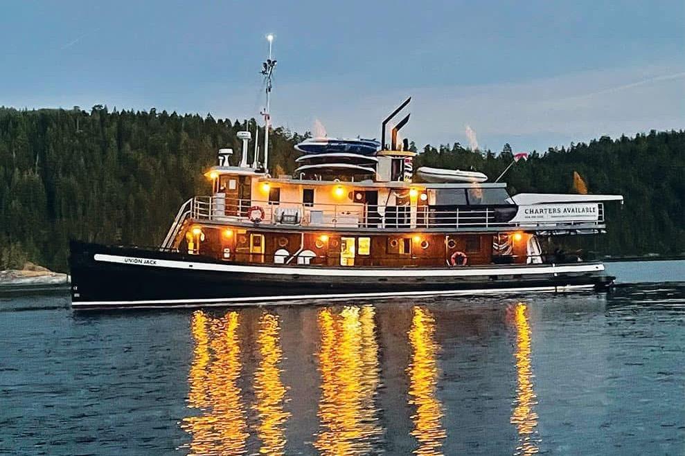 Vintage 1941 McKenzie tugboat on serene water, illuminated at dusk, with forested backdrop.