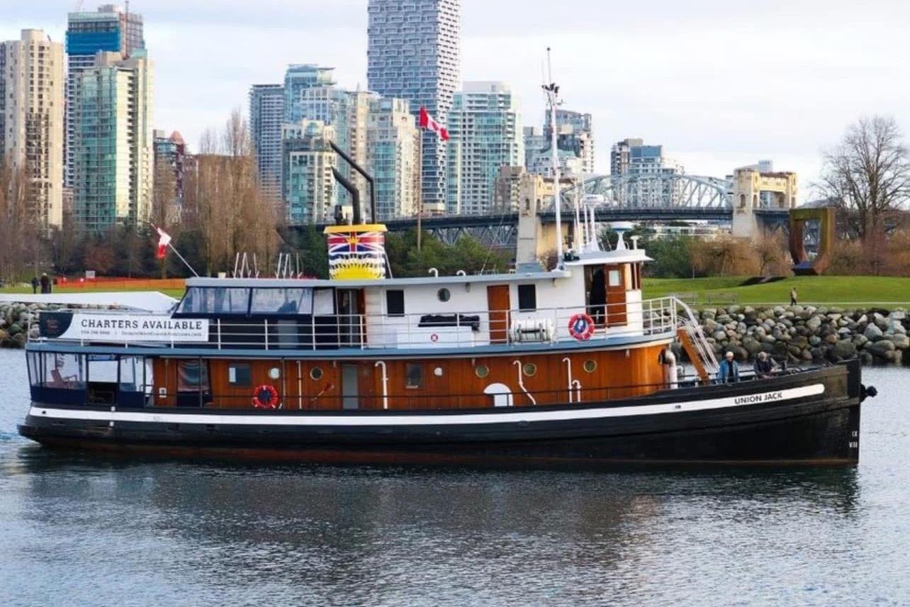 Historic 1941 McKenzie Barge tugboat "Union Jack" in urban waterfront setting, charters available.
