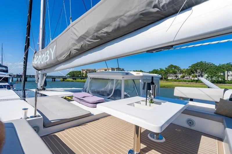 Scooby Yacht Photos Pics Luxurious 2022 Leopard 50 yacht deck with seating and table, docked by scenic waterfront.