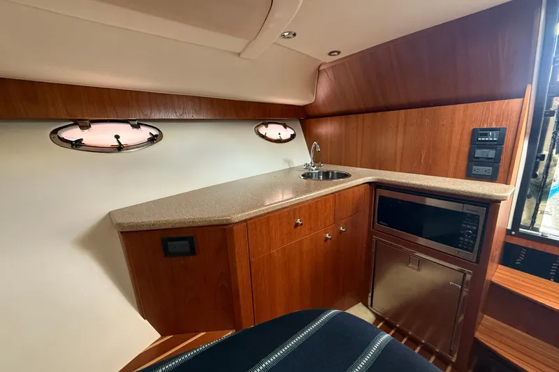 Yacht Photos Pics 2012 Tiara Yachts 3100 Coronet interior with kitchenette, featuring wood cabinetry and porthole windows.