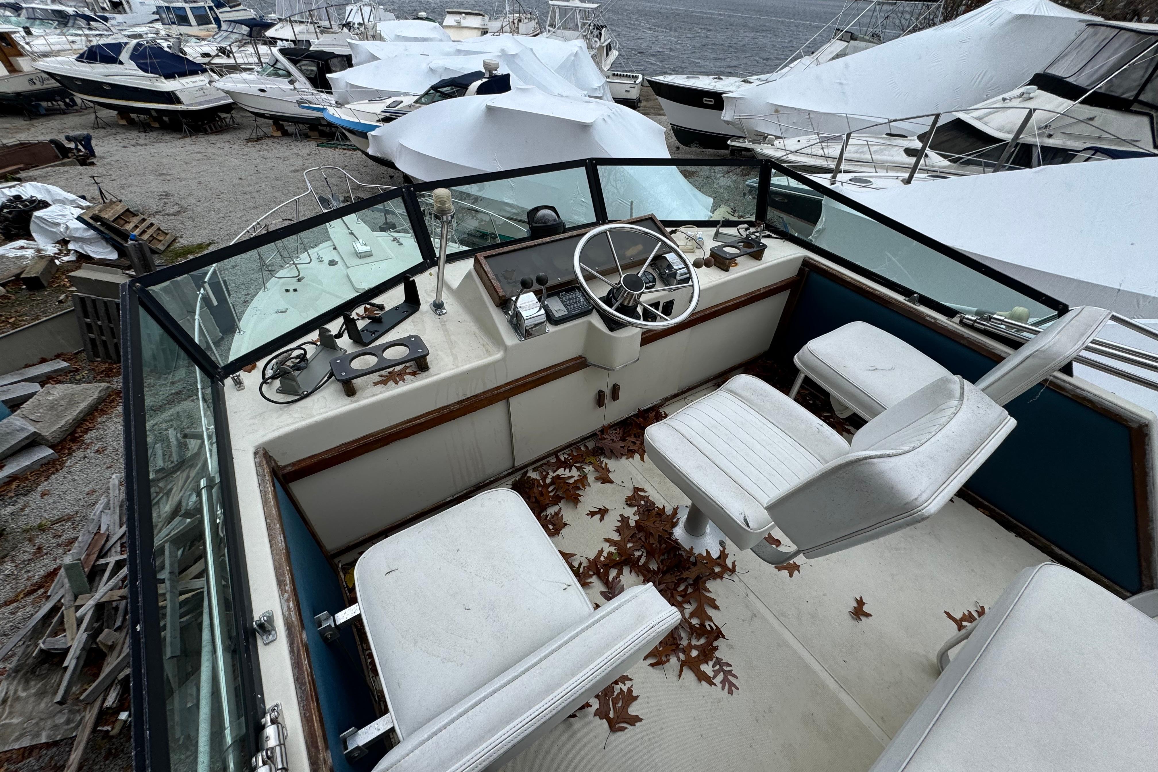 1986 Stamas Flybridge Sedan boat interior with steering wheel, seats, and fallen leaves.