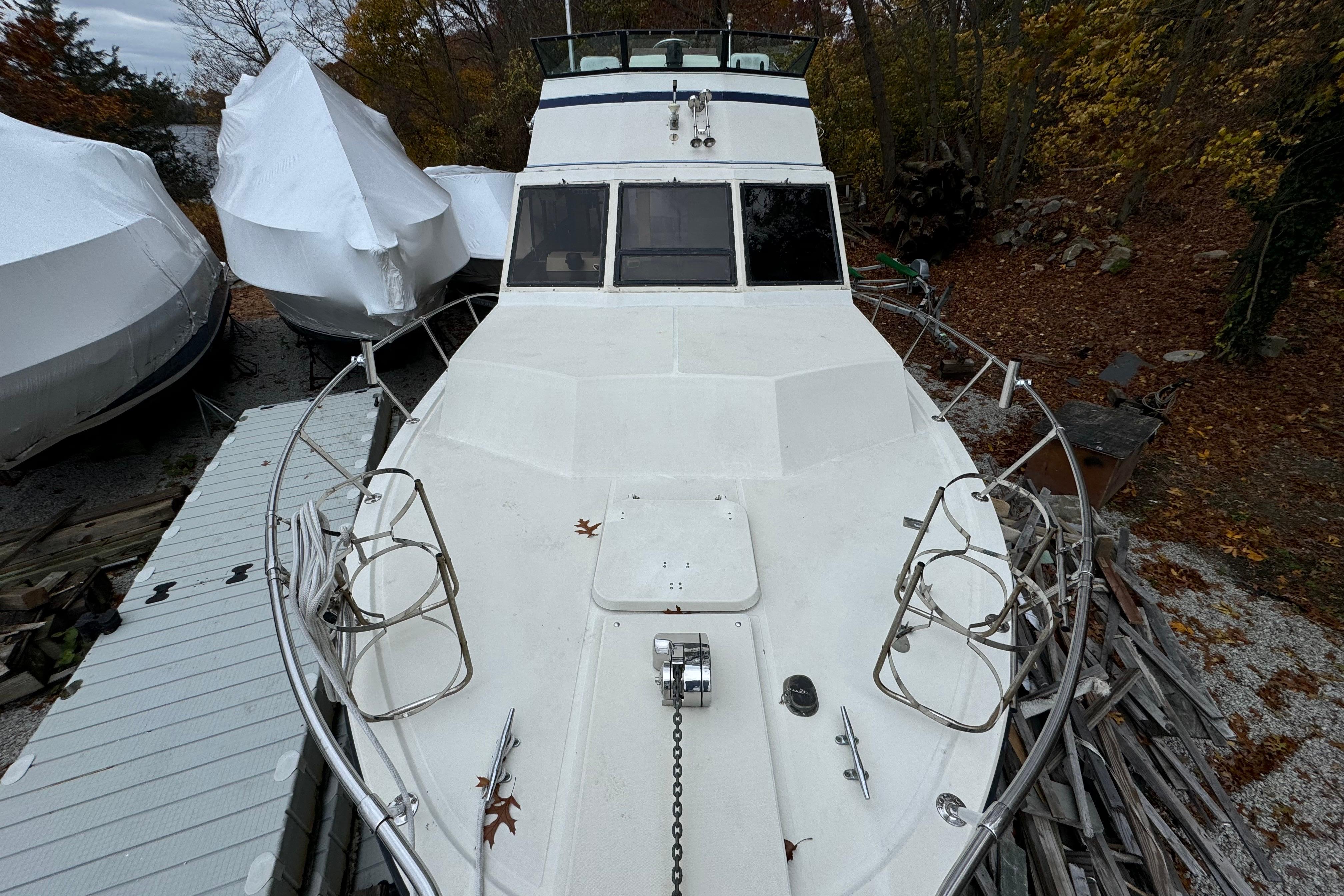 1986 Stamas Flybridge Sedan boat on land, surrounded by autumn foliage and covered vessels.