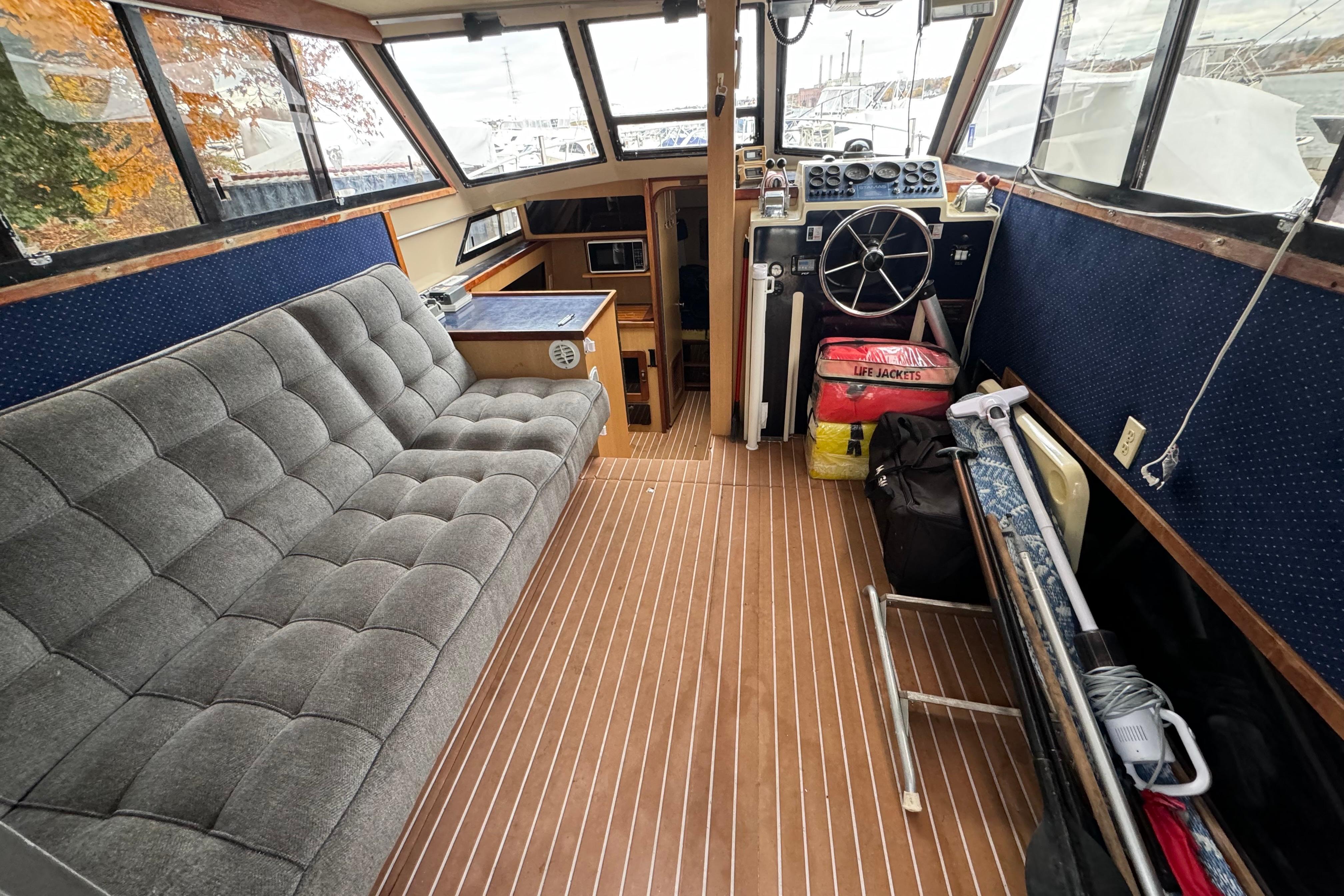 1986 Stamas Flybridge Sedan interior with gray seating, wooden flooring, and navigation controls.