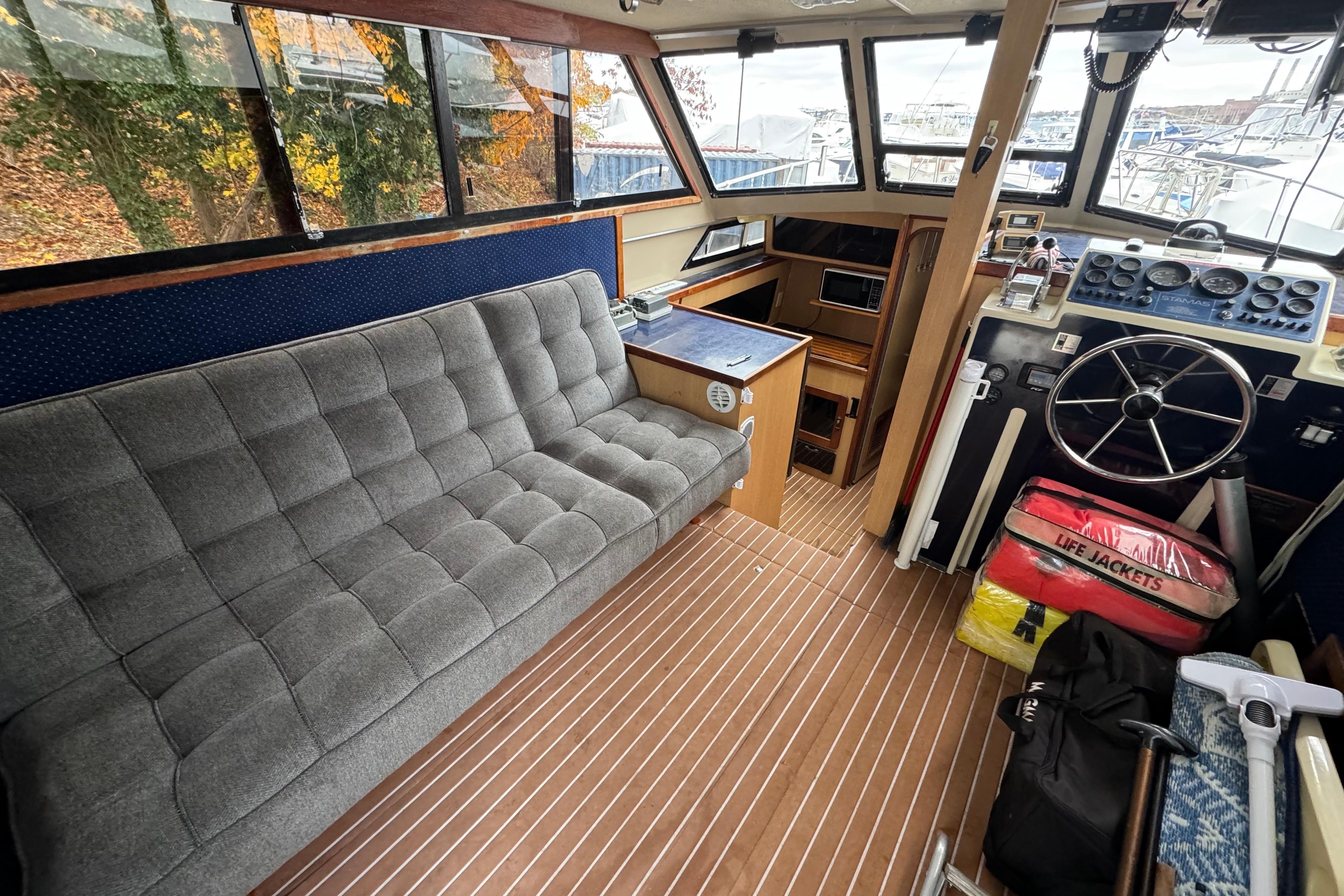 1986 Stamas Flybridge Sedan interior with gray sofa, steering wheel, and life jackets.
