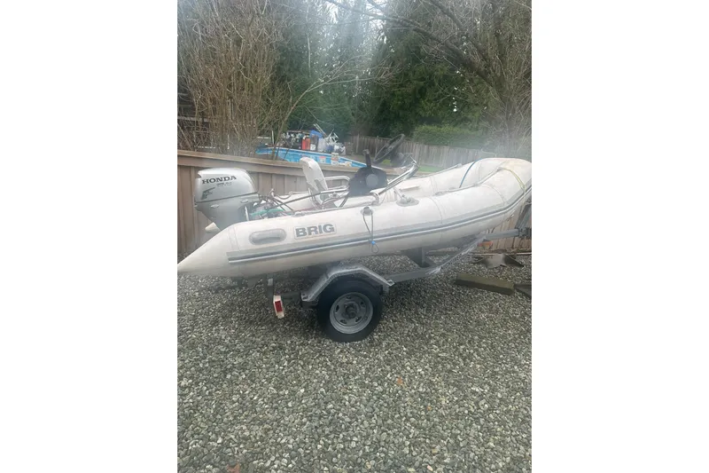 Mokikem Yacht Photos Pics Inflatable Brig boat with Honda outboard motor on a trailer, parked on gravel.