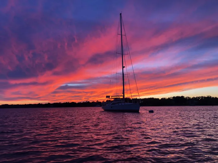 Pneumatic Yacht Photos Pics Sailboat on water at sunset with vibrant pink and purple sky, Outbound 56, 2020 model.