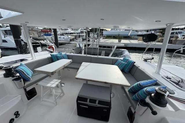 Swell Yacht Photos Pics 2021 Outremer 51 catamaran cockpit with seating, tables, and striped cushions at a marina.