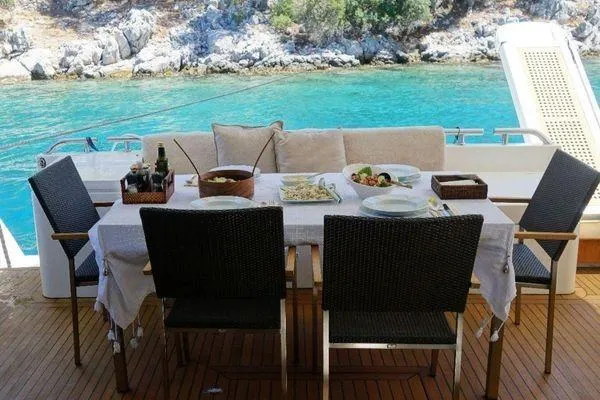 Golden Ex Yacht Photos Pics Outdoor dining setup on 2001 Ferretti Yachts 680, overlooking turquoise waters and rocky shoreline.
