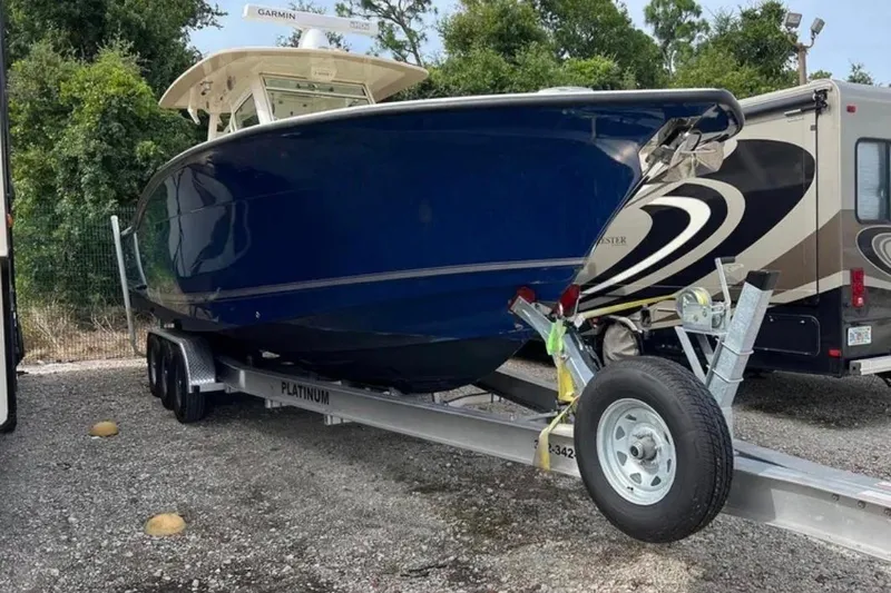  Yacht Photos Pics 2017 Scout 350 LXF boat on trailer, parked beside RV, surrounded by trees.