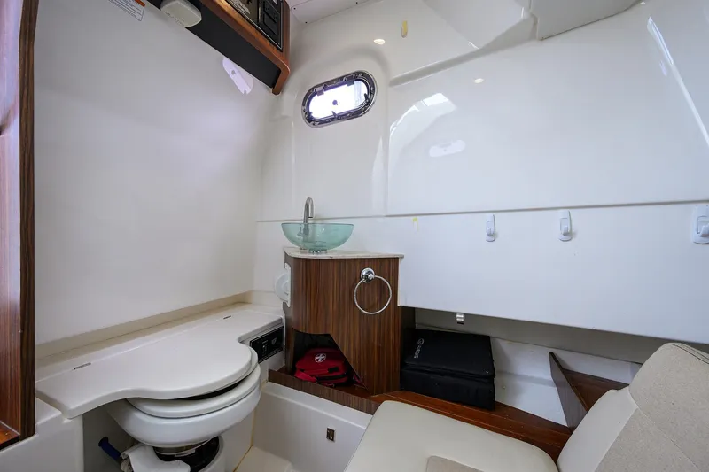  Yacht Photos Pics 2019 Pursuit S 328 Sport boat interior with toilet, sink, and wooden cabinetry.