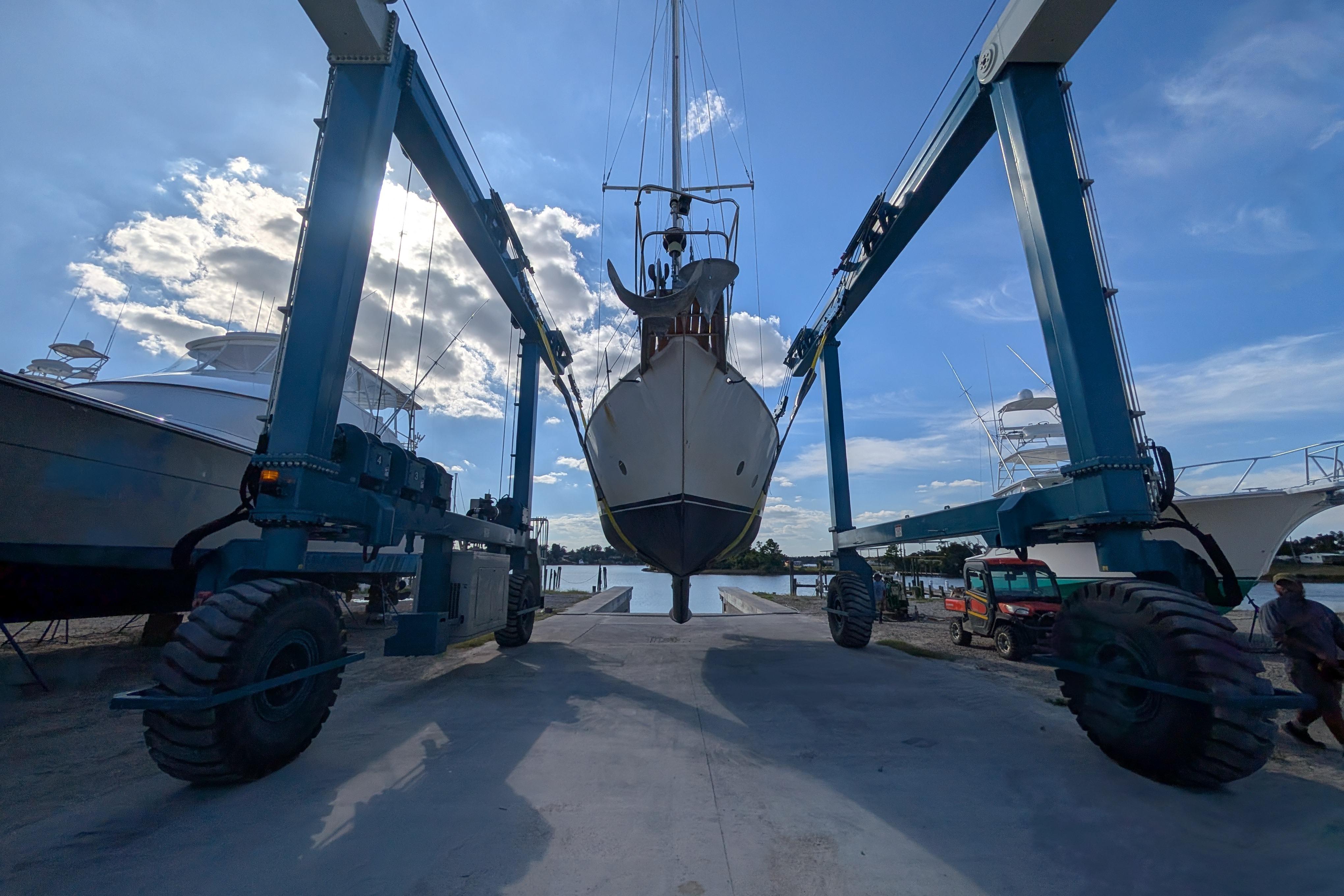 Bruce Bingham Custom 47 Steel Hull 1992 sailboat lifted by boat hoist under blue sky.