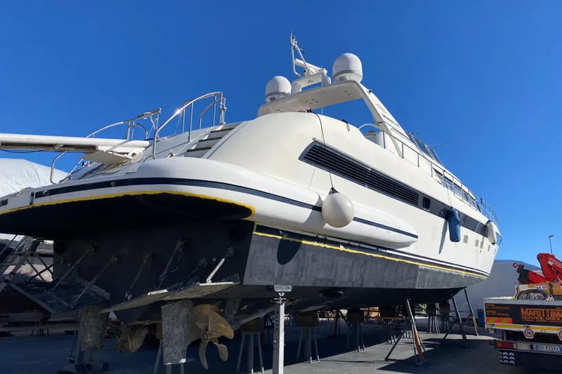  Yacht Photos Pics 1996 Overmarine Mangusta 100 yacht on dry dock, showcasing hull and propellers under clear blue sky.