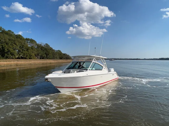  Yacht Photos Pics 2024 Pursuit DC 266 Dual Console boat cruising on a calm lake under a clear blue sky.