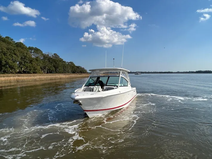  Yacht Photos Pics 2024 Pursuit DC 266 Dual Console boat cruising on a calm river under a clear blue sky.