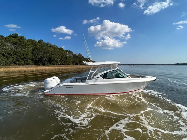  Yacht Photos Pics 2024 Pursuit DC 266 Dual Console boat cruising on a calm lake under a clear blue sky.