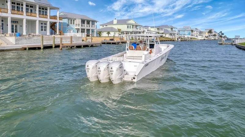 Aqua Toy Yacht Photos Pics 2023 Jupiter 43 Center Console boat cruising near waterfront homes under a clear blue sky.