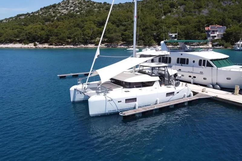 Jack Yacht Photos Pics 2024 Lagoon 42 catamaran docked in serene marina with lush green backdrop.