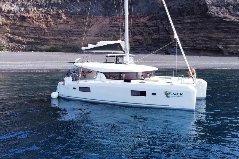 Jack Yacht Photos Pics 2024 Lagoon 42 catamaran anchored near rocky shoreline, calm blue waters.