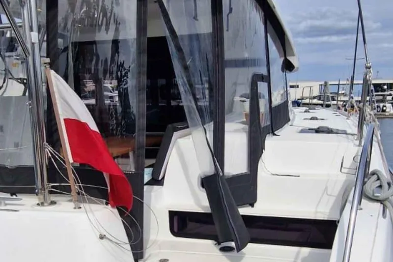  Yacht Photos Pics 2024 Lagoon 42 catamaran with a red and white flag, docked at a marina.