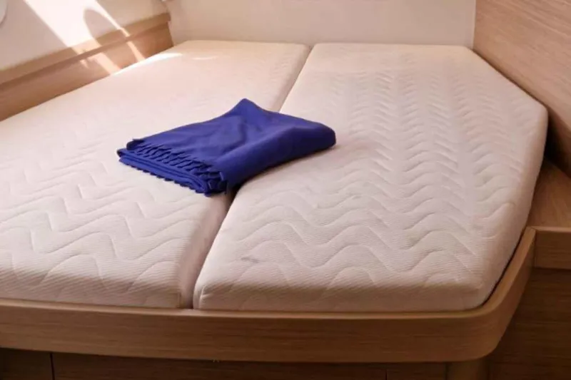  Yacht Photos Pics 2024 Lagoon 42 yacht interior with twin mattresses and a folded blue blanket.