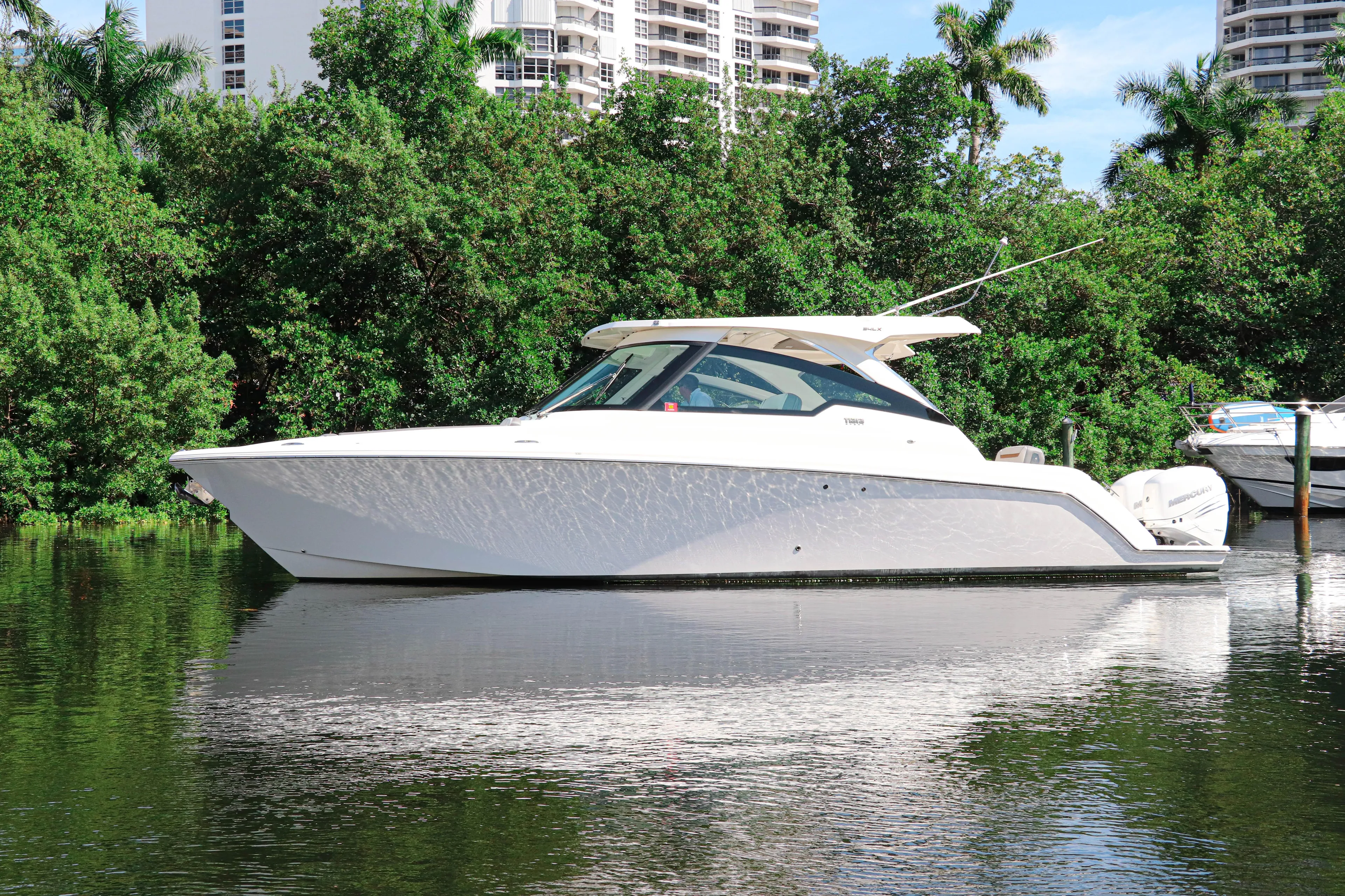  Yacht Photos Pics 2021 Tiara Sport 34 LX boat on calm water, surrounded by lush greenery.