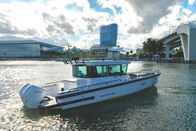 Squirt Yacht Photos Pics 2023 Axopar 28 CABIN boat on water near modern buildings and bridge.