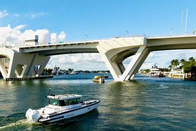 Squirt Yacht Photos Pics 2023 Axopar 28 CABIN boat cruising under a modern bridge on a sunny day.